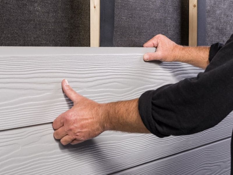 Technicien procédant à l'installation d'un bardage ventilé afin d'isoler une maison de l'extérieur.