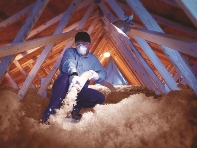 Technicien qui effectue l'isolation des combles en utilisant de la laine de verre en vrac Knauf.