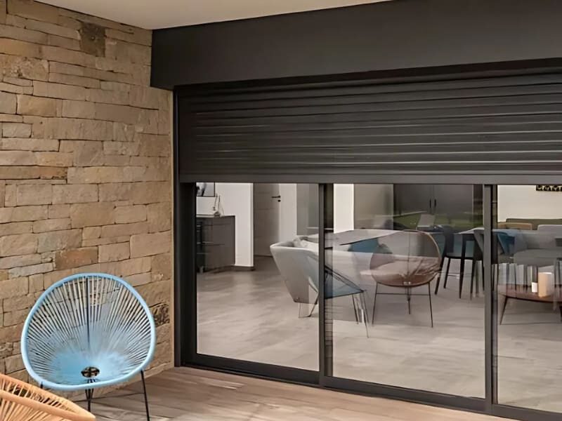 Photo extérieure d'une porte vitré avec des volets roulants en aluminium de couleur noire au un tier baissés.